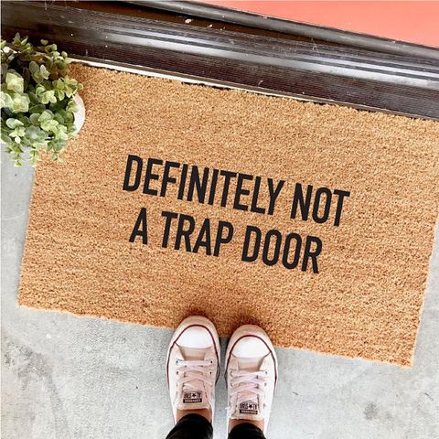picture of a welcome mat that has "Definitely Not A Trap Door" printed on it. 